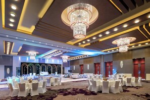 A spacious banquet hall with round tables, chandeliers, and a stage.