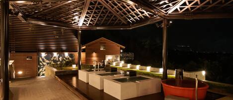 A covered outdoor area with a pool, seating, and a wooden building in the background.