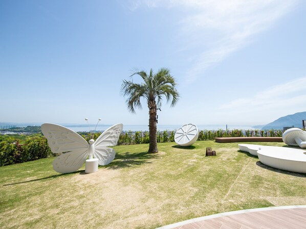 Un área exterior ajardinada con una palmera, una gran escultura blanca que recuerda a las alas de una mariposa, y un espacio de estar circular.