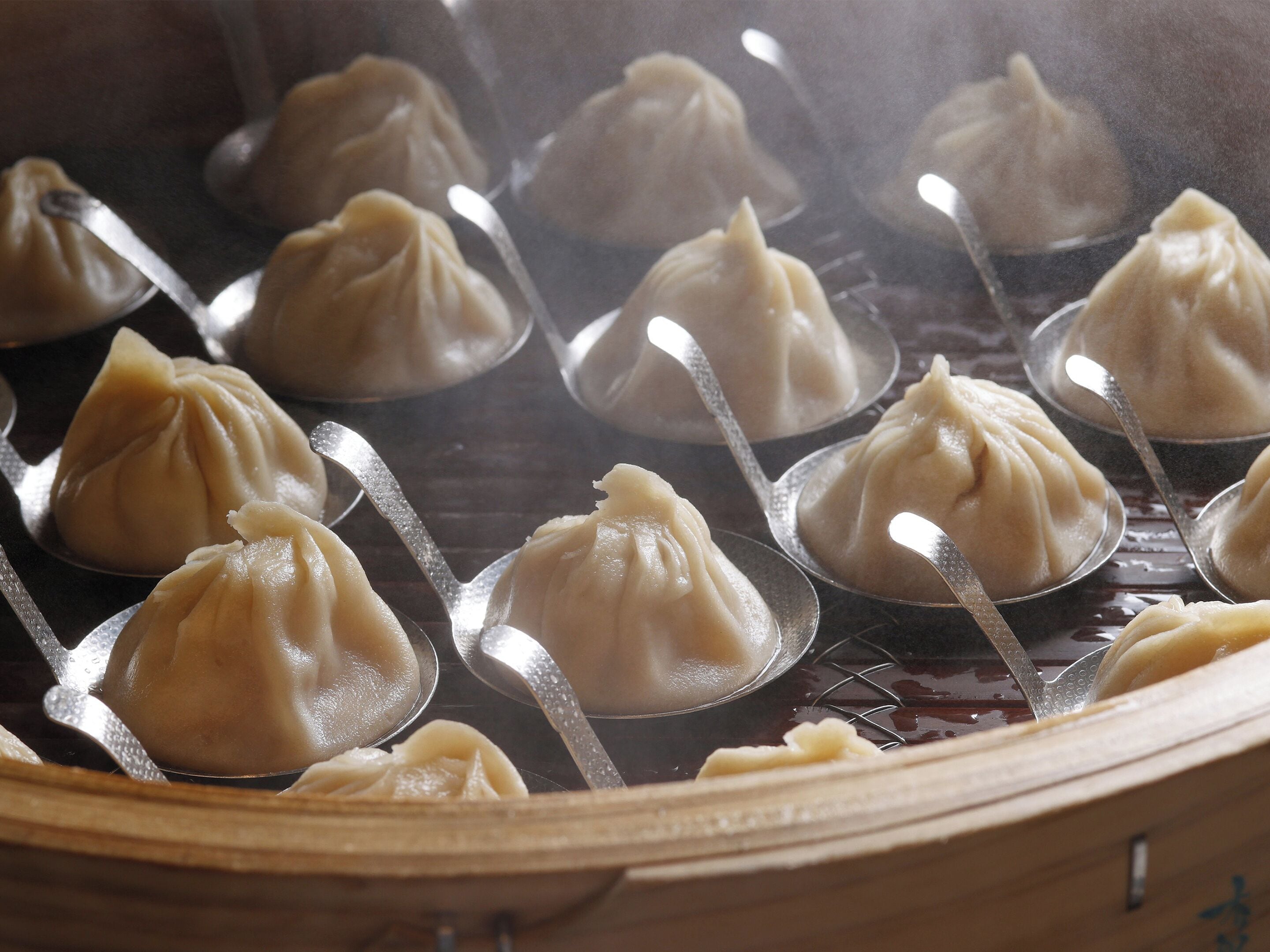 Una vaporera con varios dumplings en cucharas metálicas.