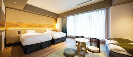 Une chambre d’hôtel avec deux lits, un coin salon avec une table et des chaises, et une grande fenêtre avec des rideaux.