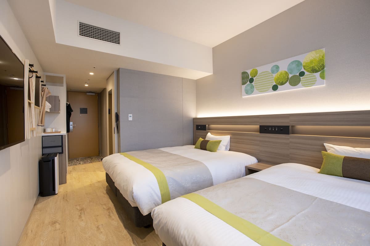 Hotellihuone, jossa on kaksi sänkyä, työpöytä, vaatekaappi ja kylpyhuone.