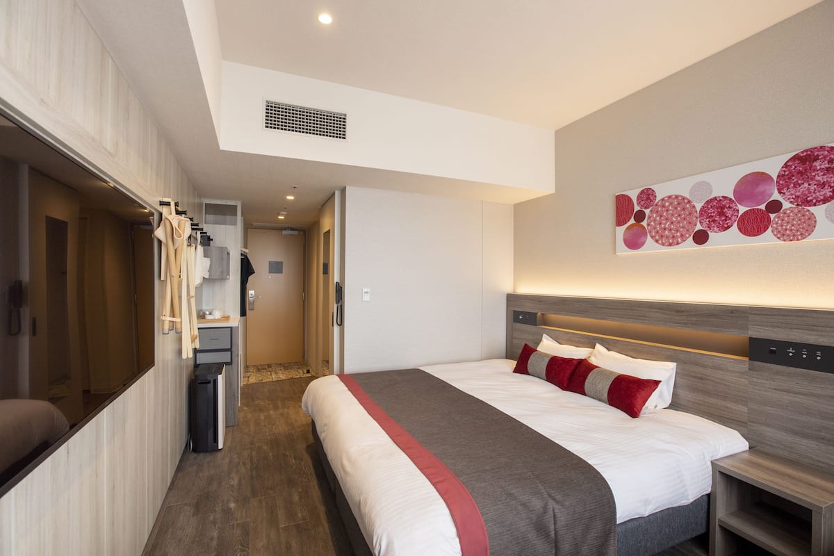 Moderni hotellihuone, jossa on suuri sänky, vaatekaappi, työpöytä ja kylpyhuone.