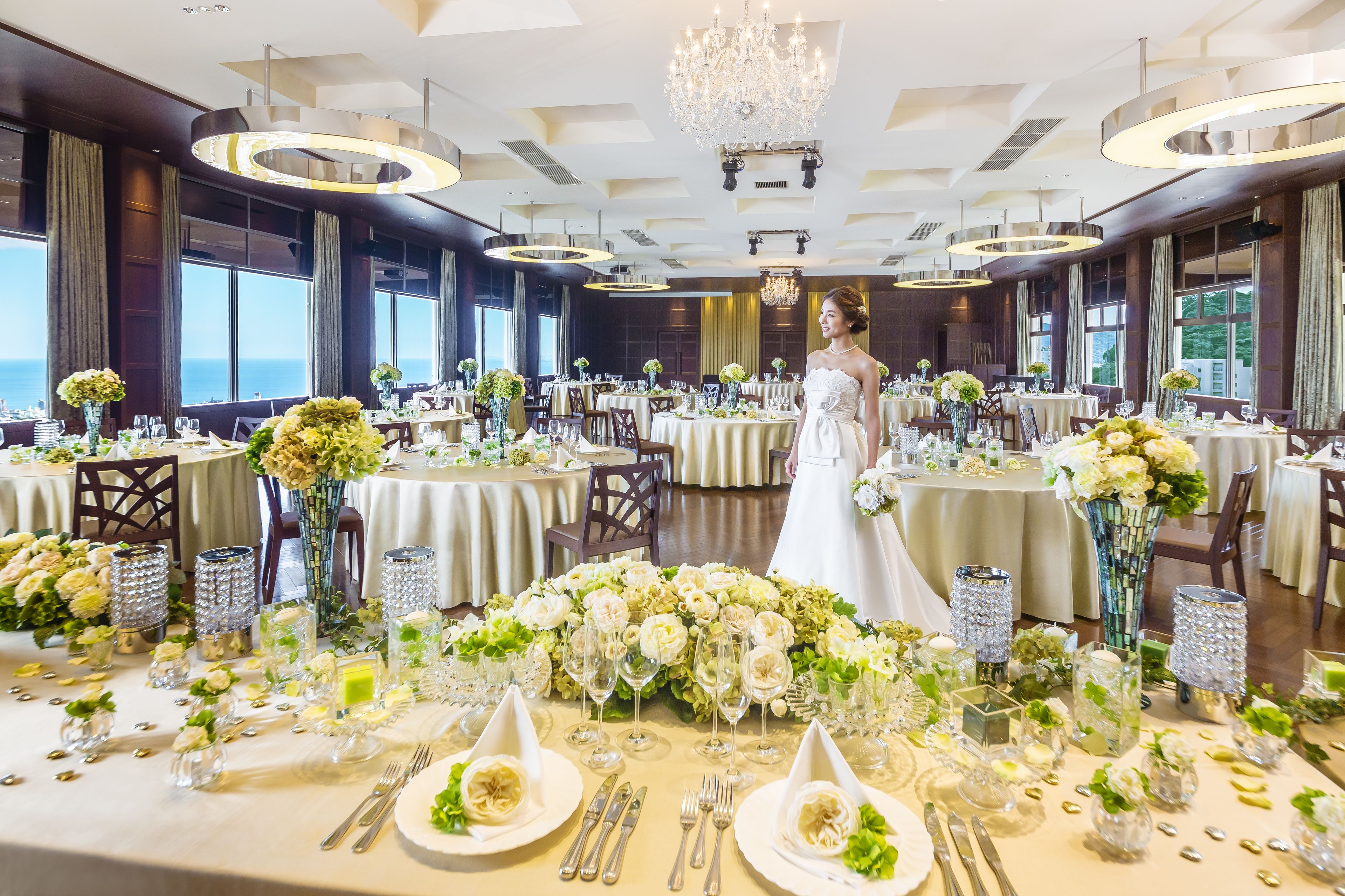 A banquet hall with round tables set for a wedding, featuring floral centerpieces and elegant table settings.