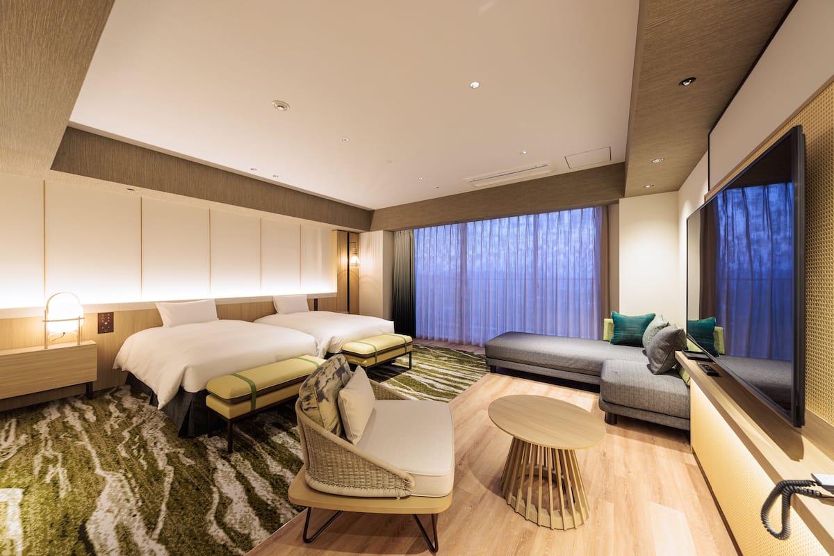 Moderni hotellihuone, jossa on suuri sänky, sohva, tuoli, pieni pöytä ja televisio.