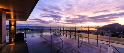 A modern building with a glass facade overlooking a cityscape and a body of water at sunset.
