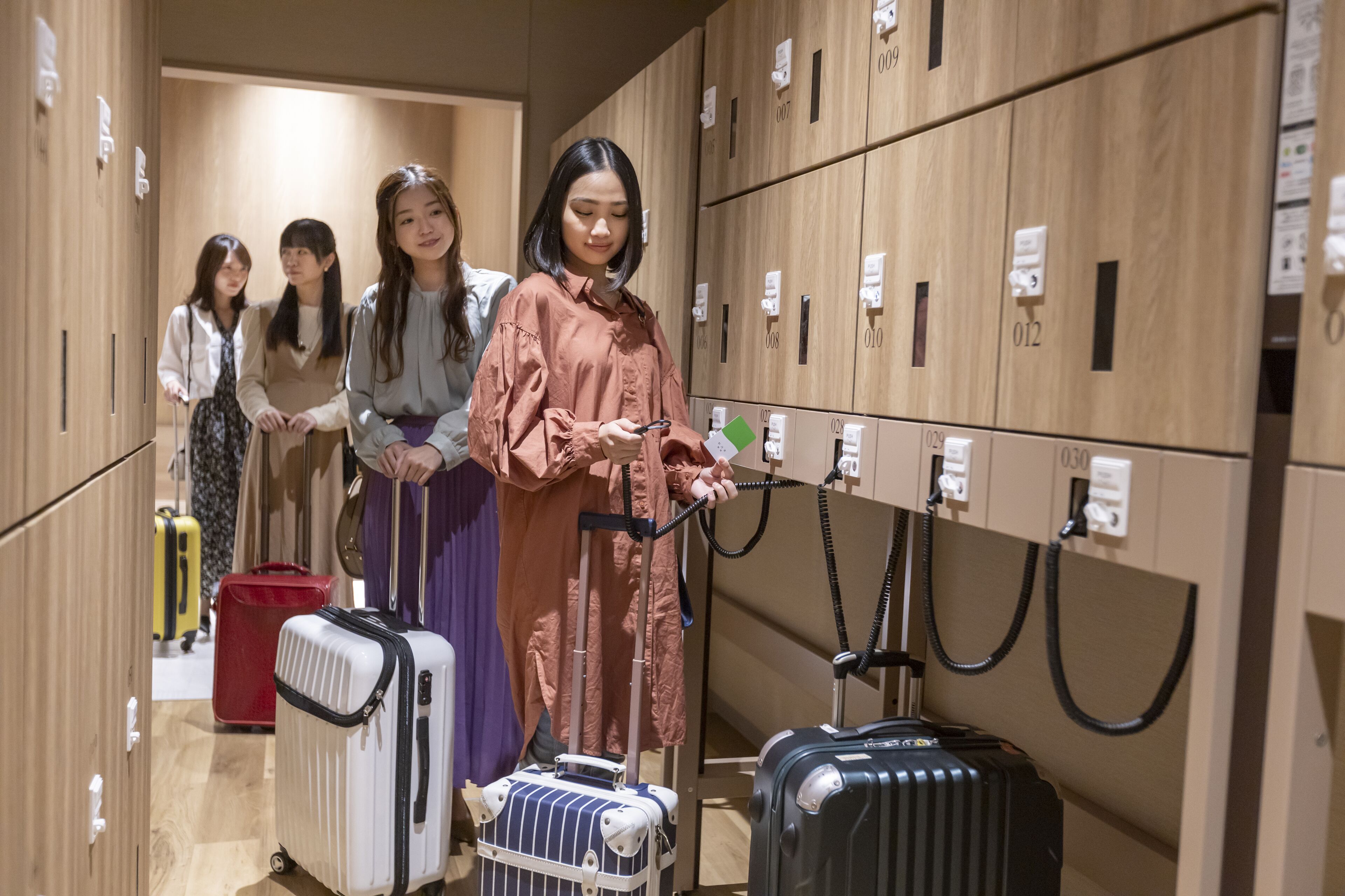 A hotel lobby with wooden lockers, a woman using a phone, and several suitcases.