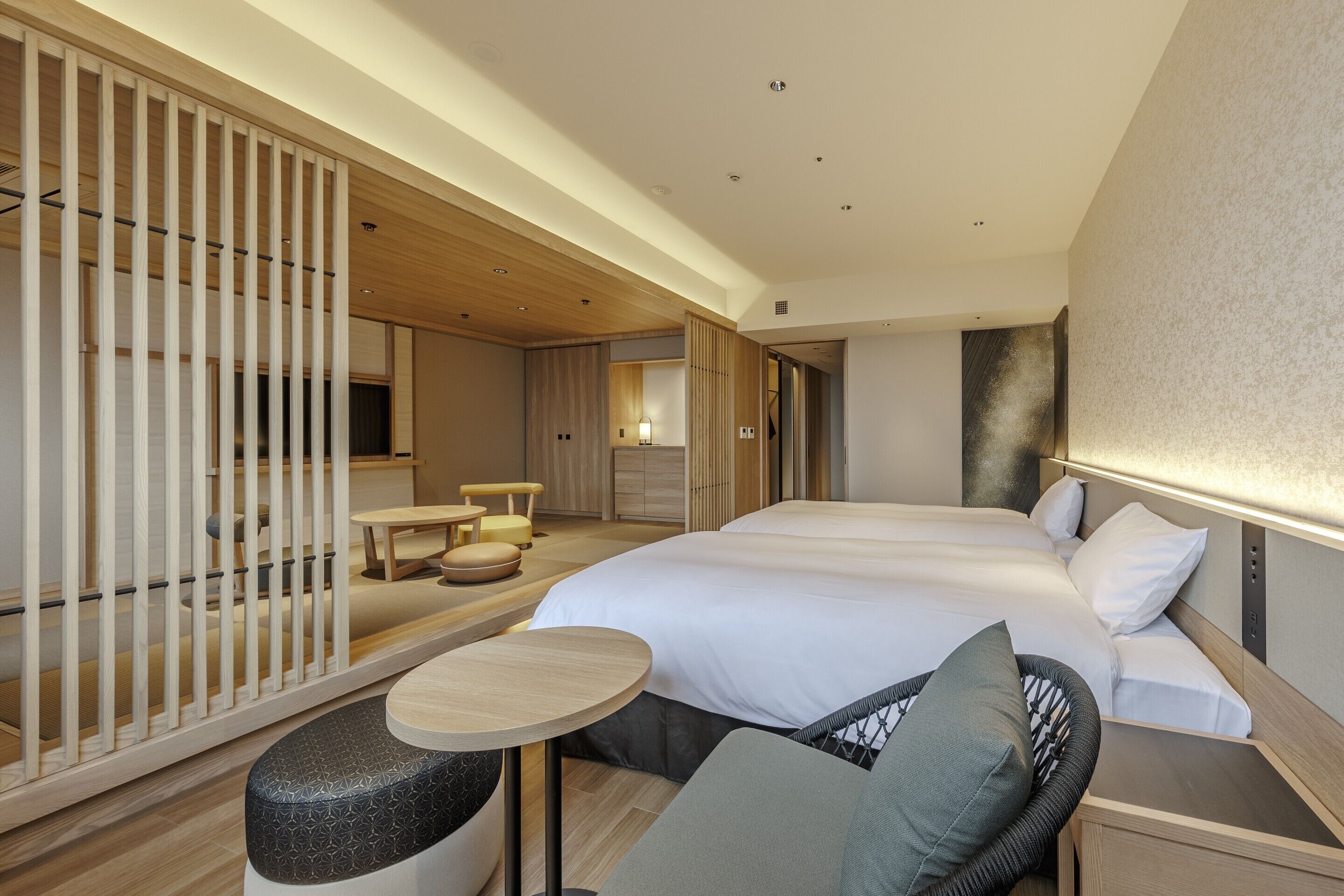Una habitación de hotel moderna con una cama grande, un espacio de descanso con una mesa redonda y una zona de dormir separada con un sofá.