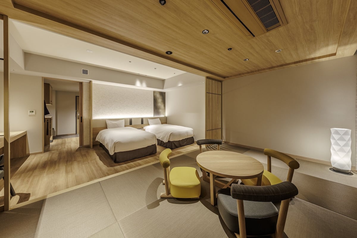 Moderni hotellihuone, jossa on kaksi sänkyä, ruokailutila ja pieni keittiö.