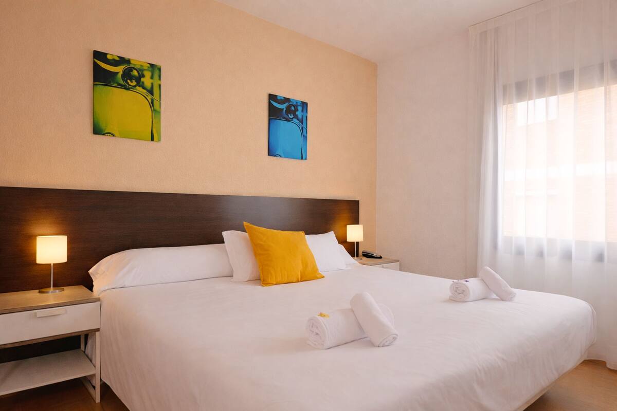 A hotel room with a large bed, a nightstand, a lamp, and two paintings on the wall.