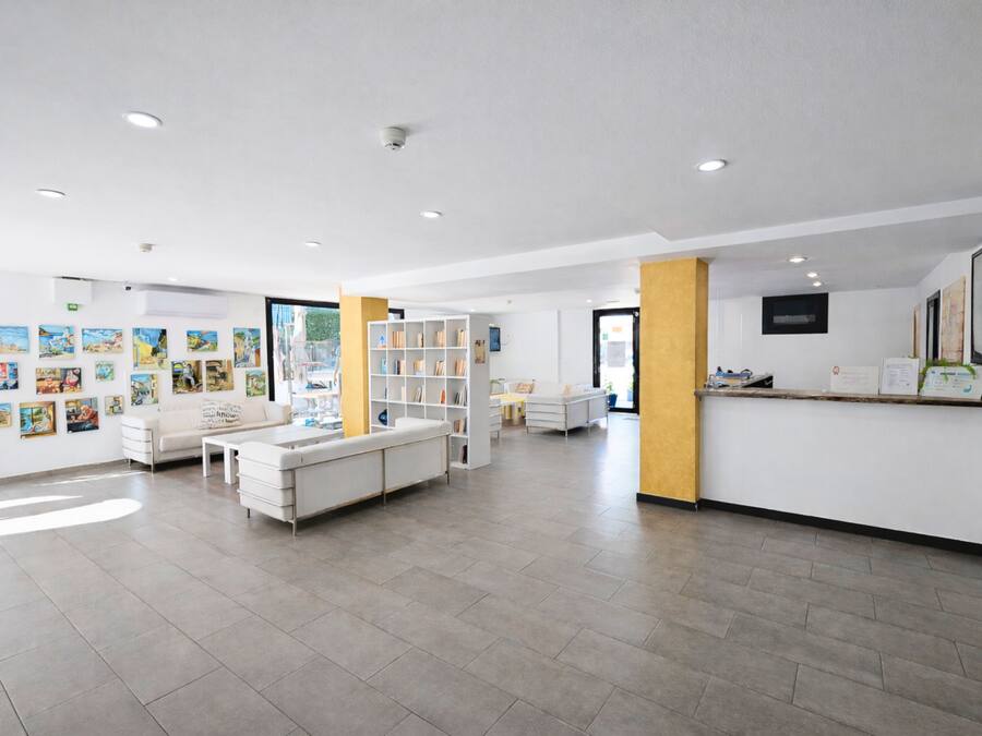 A spacious lobby with a white reception desk, a bookshelf, and a seating area with a sofa and chairs.