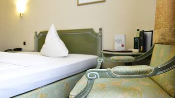 A bed with a white mattress and pillows, a green upholstered chair, a bedside table with a lamp, and a framed picture on the wall.