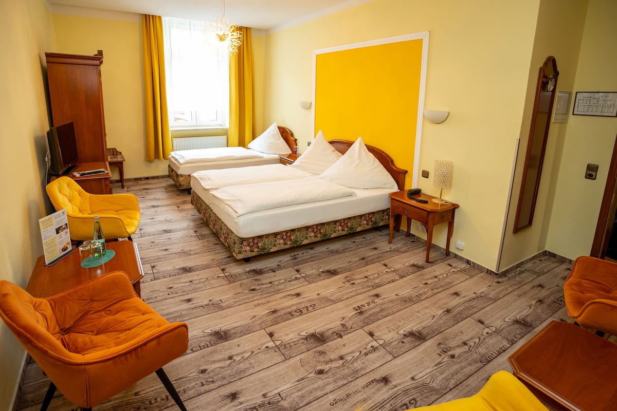 Habitación de hotel con dos camas, piso de madera, pared amarilla y una silla amarilla.
