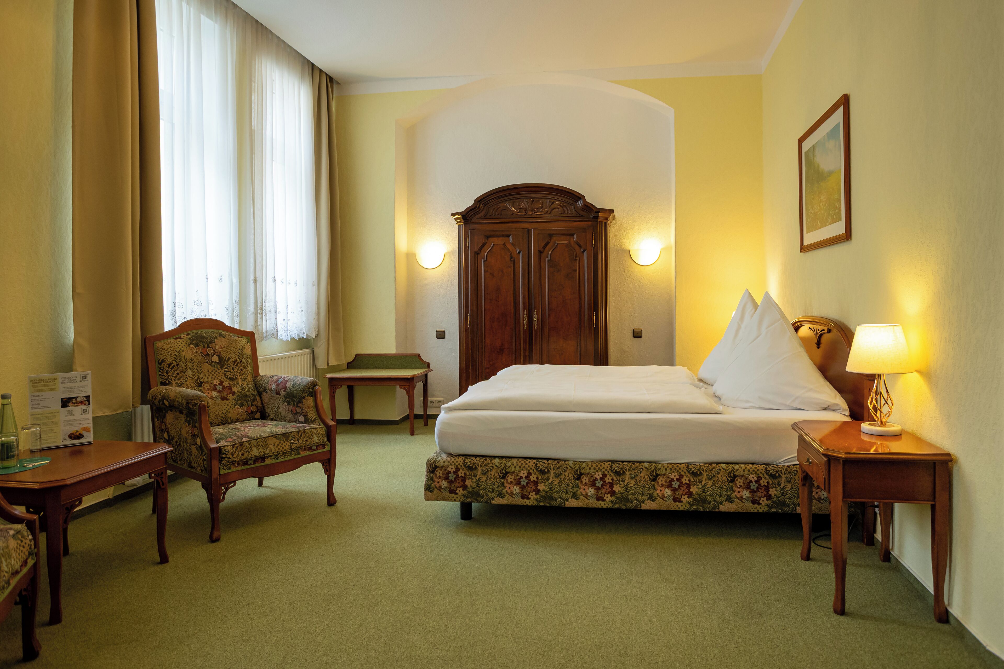 A hotel room with a bed, a chair, a nightstand, and a lamp.