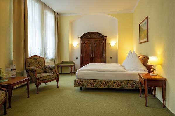 A hotel room with a bed, a chair, a nightstand, and a lamp.