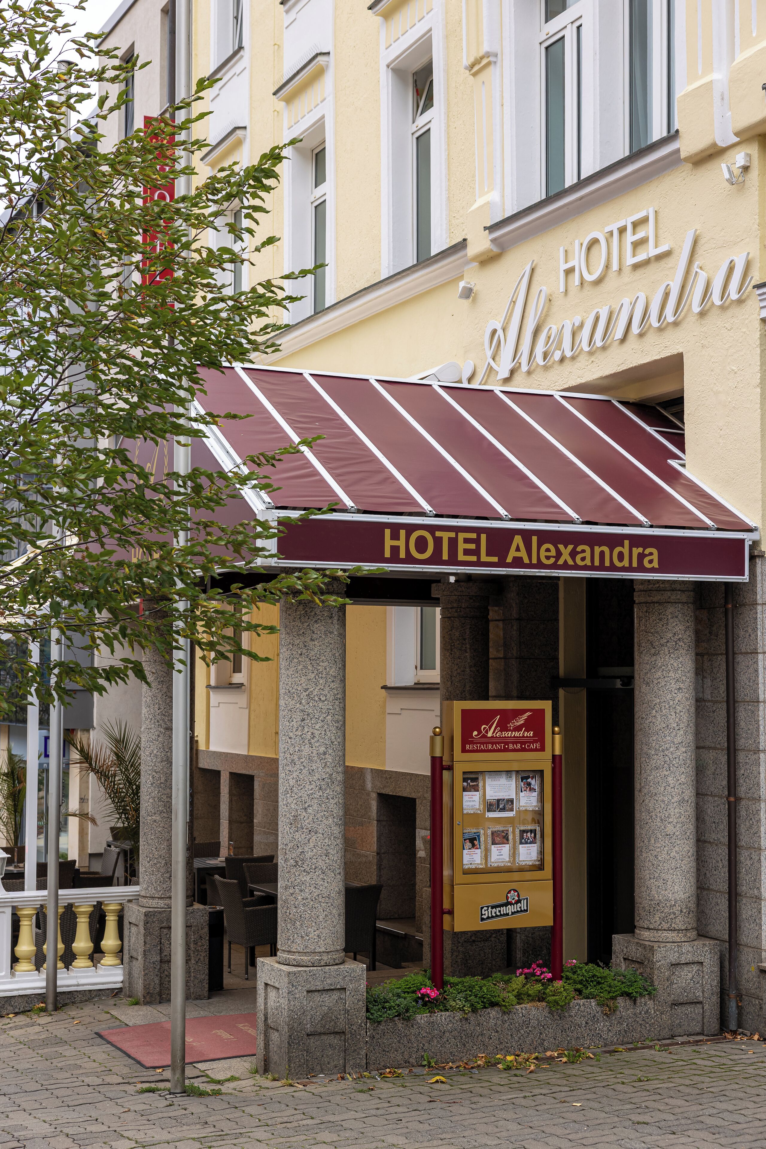 Hotel HOTEL Alexandra con tenda color borgogna, colonne in pietra e insegna per ristorante, bar e caffetteria.