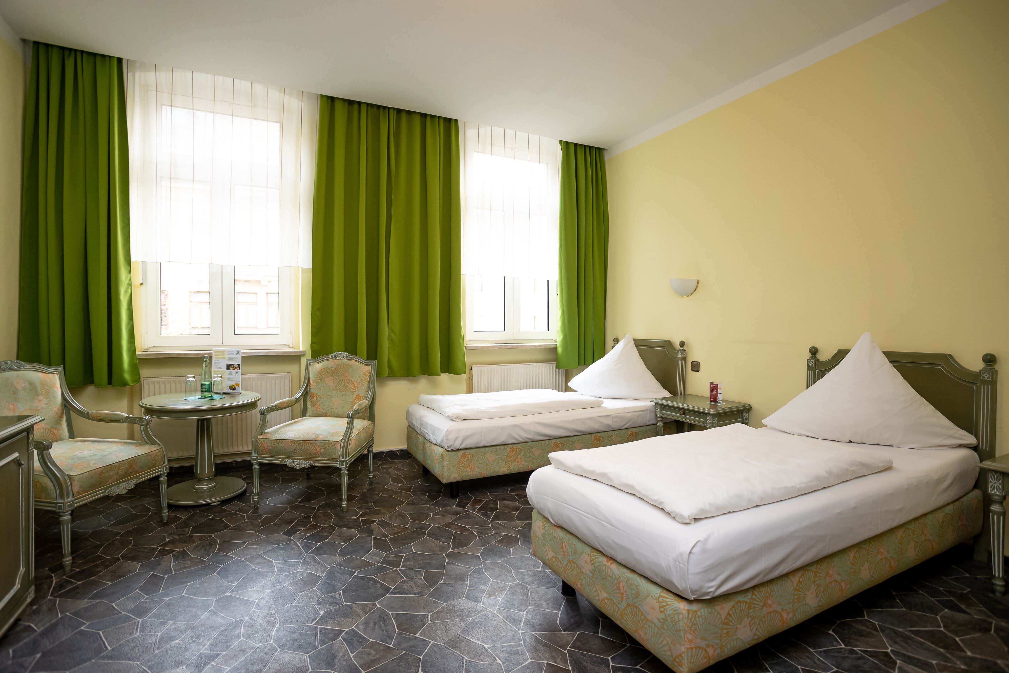 Habitación de hotel con dos camas individuales, una mesita redonda, dos sillas y un radiador.