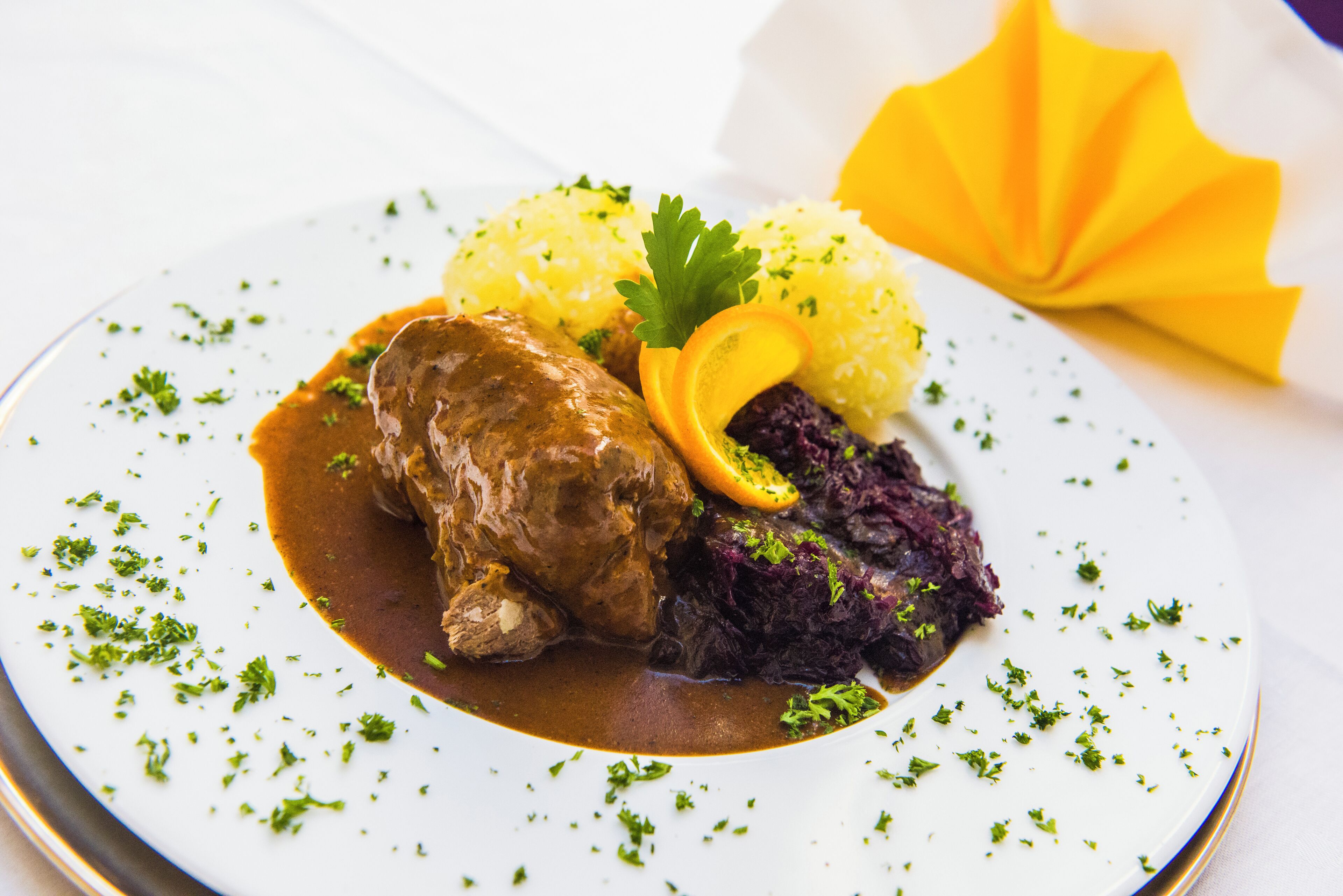 Un plato con un guiso de carne, arroz amarillo y col roja, adornado con perejil y una rodaja de naranja.