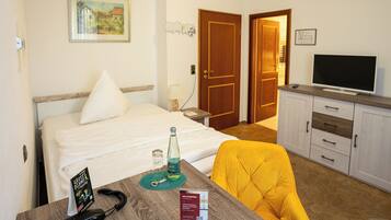 A hotel room with a bed, a desk with a chair, a television, and a door leading to another room.