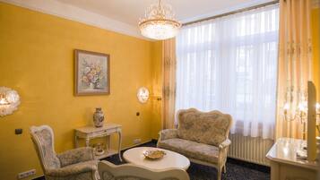 Una habitación con pared amarilla, un candelabro, dos sillones, una mesita y un cuadro.