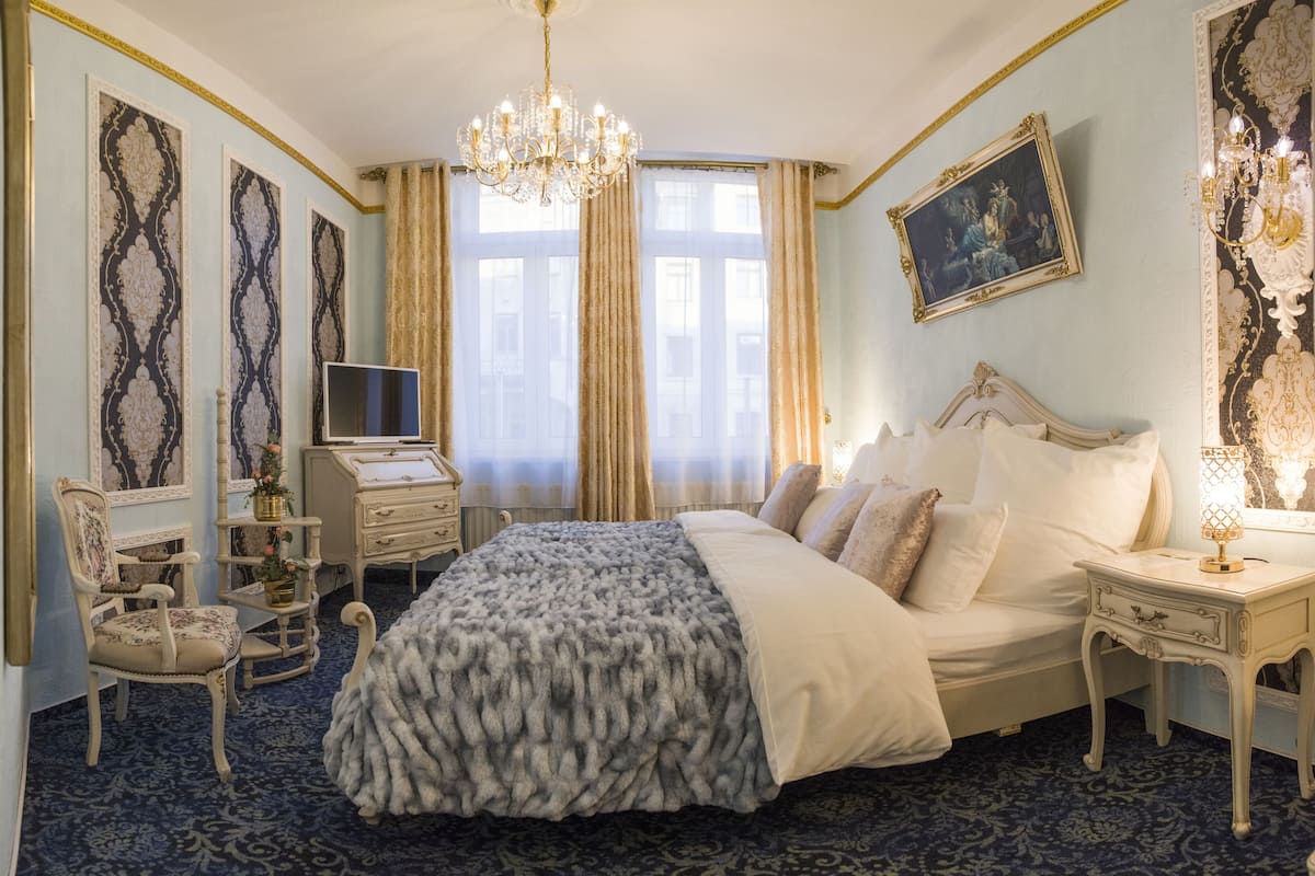 Un dormitorio clásico y elegantemente amoblado, con una cama grande, un escritorio, una silla y una araña.