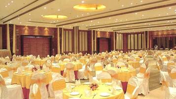 Un amplio salón de banquetes con mesas redondas cubiertas con manteles blancos y centros de mesa amarillos, dispuestas en filas.