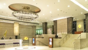 A modern lobby with a reception desk, a large chandelier, and a staircase.
