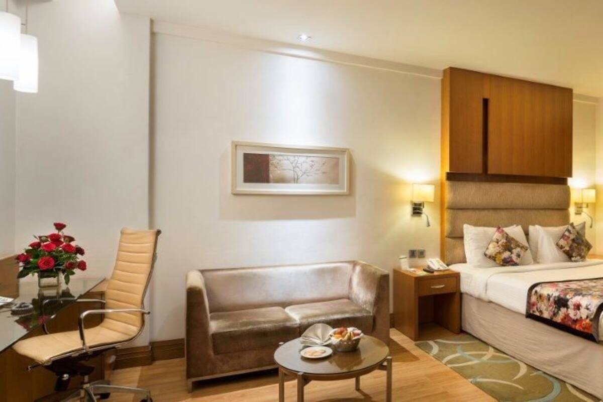 A hotel room with a bed, a sofa, a desk with a phone, and a small table with a vase of flowers.