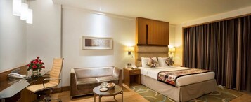 Habitación de hotel con cama, sofá, escritorio con teléfono y una mesita con un jarrón de flores.