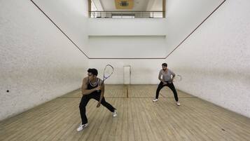 Dos personas jugando al squash en una sala con techo alto y suelo de madera.