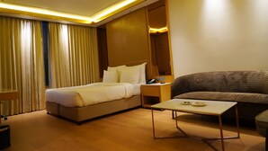 A hotel room with a bed, a sofa, a bedside table, and a small table with a phone and a plate.