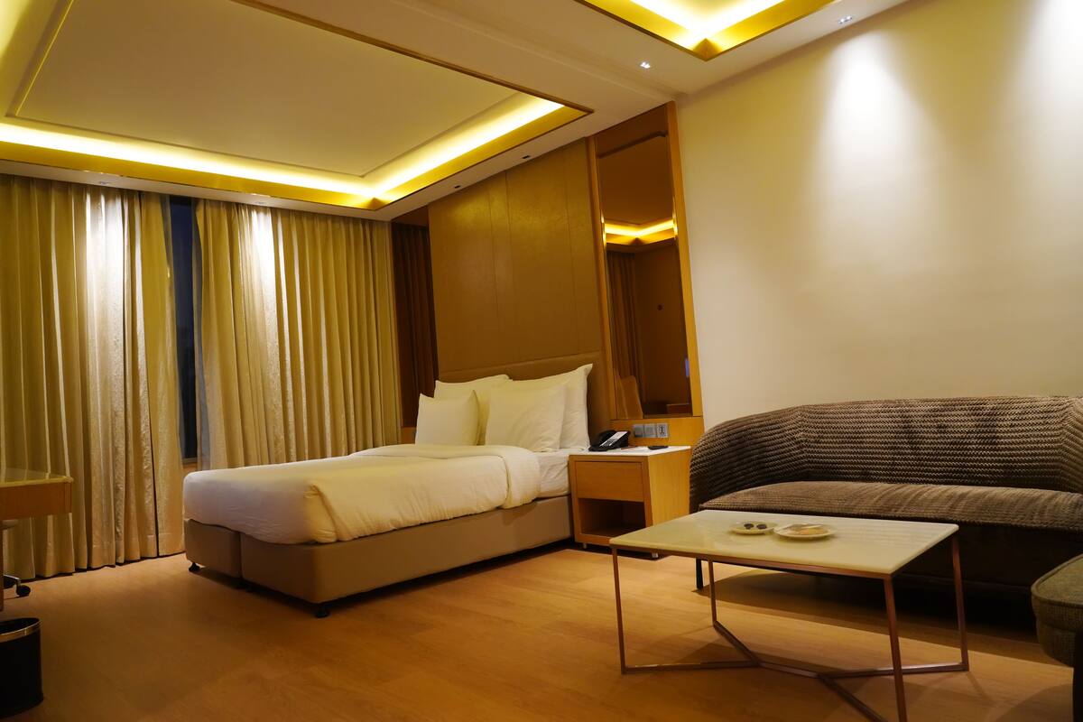 A hotel room with a bed, a sofa, a bedside table, and a small table with a phone and a plate.