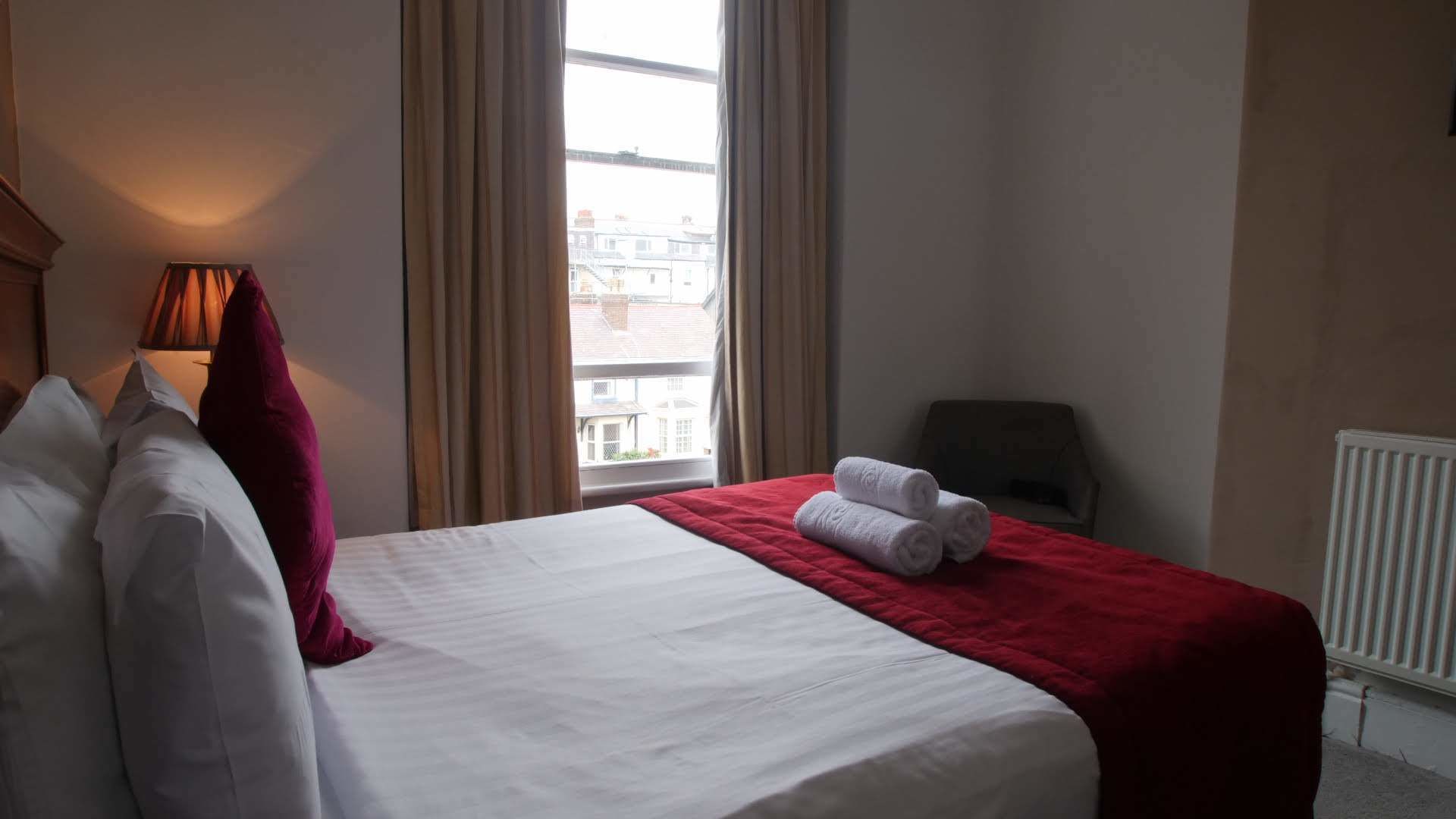 Una habitación de hotel con cama, ventana con cortinas, un radiador y una silla.