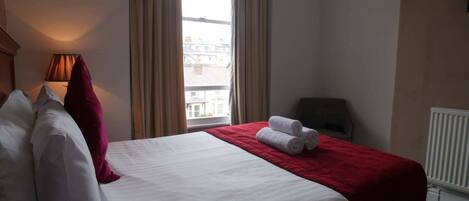 Una habitación de hotel con cama, ventana con cortinas, un radiador y una silla.
