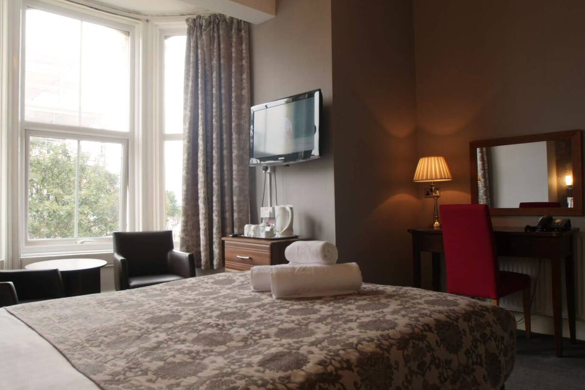 A hotel room with a bed, a desk, a chair, a television, and a window with curtains.