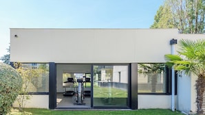 A modern building with a glass entrance, a visible gym area with exercise equipment, and a well-maintained lawn.