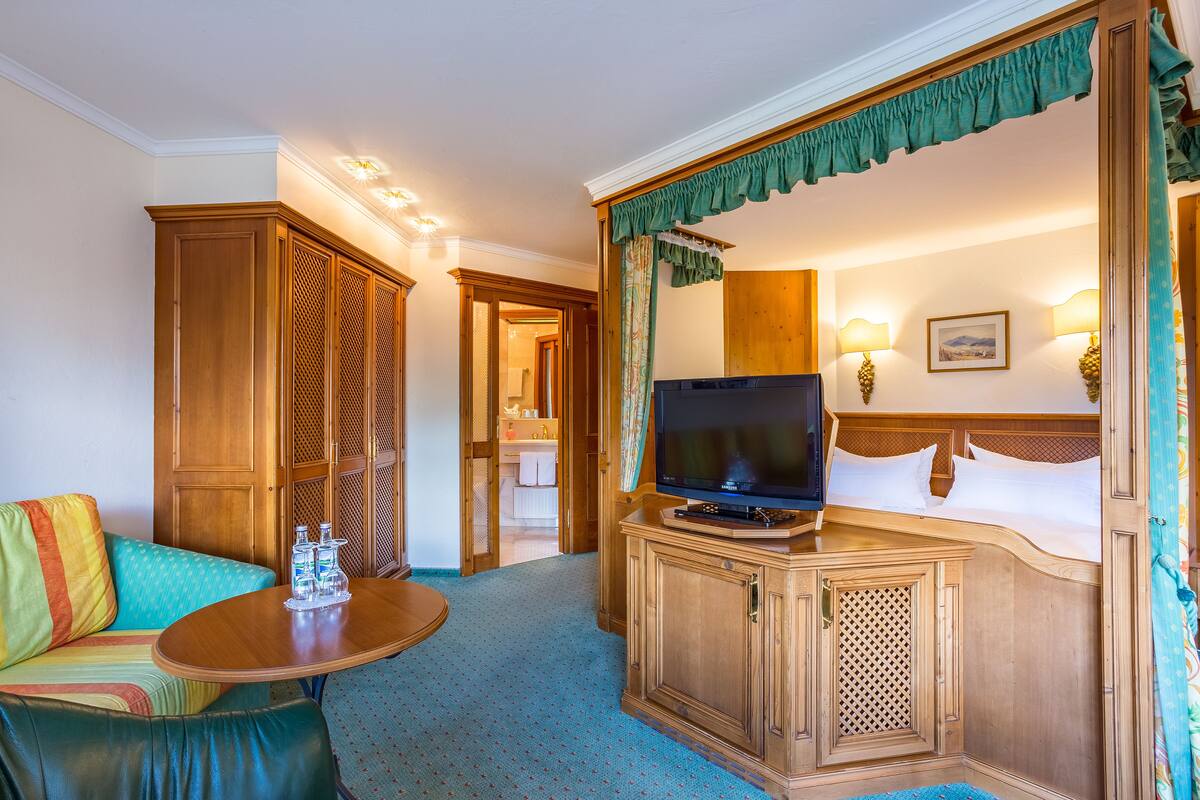 A hotel room with a television, a bed, a sofa, and a small table with water bottles.