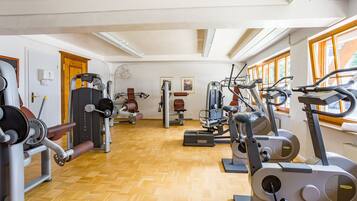 A gym with various exercise machines, wooden flooring, and large windows.