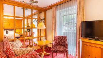 Habitación de hotel con ventanal de madera, un sofá, una silla, un televisor y una mesa con lámpara.