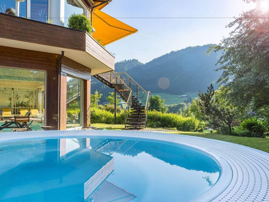 Zona de piscina moderna al aire libre con vistas despejadas a una montaña y un lago.