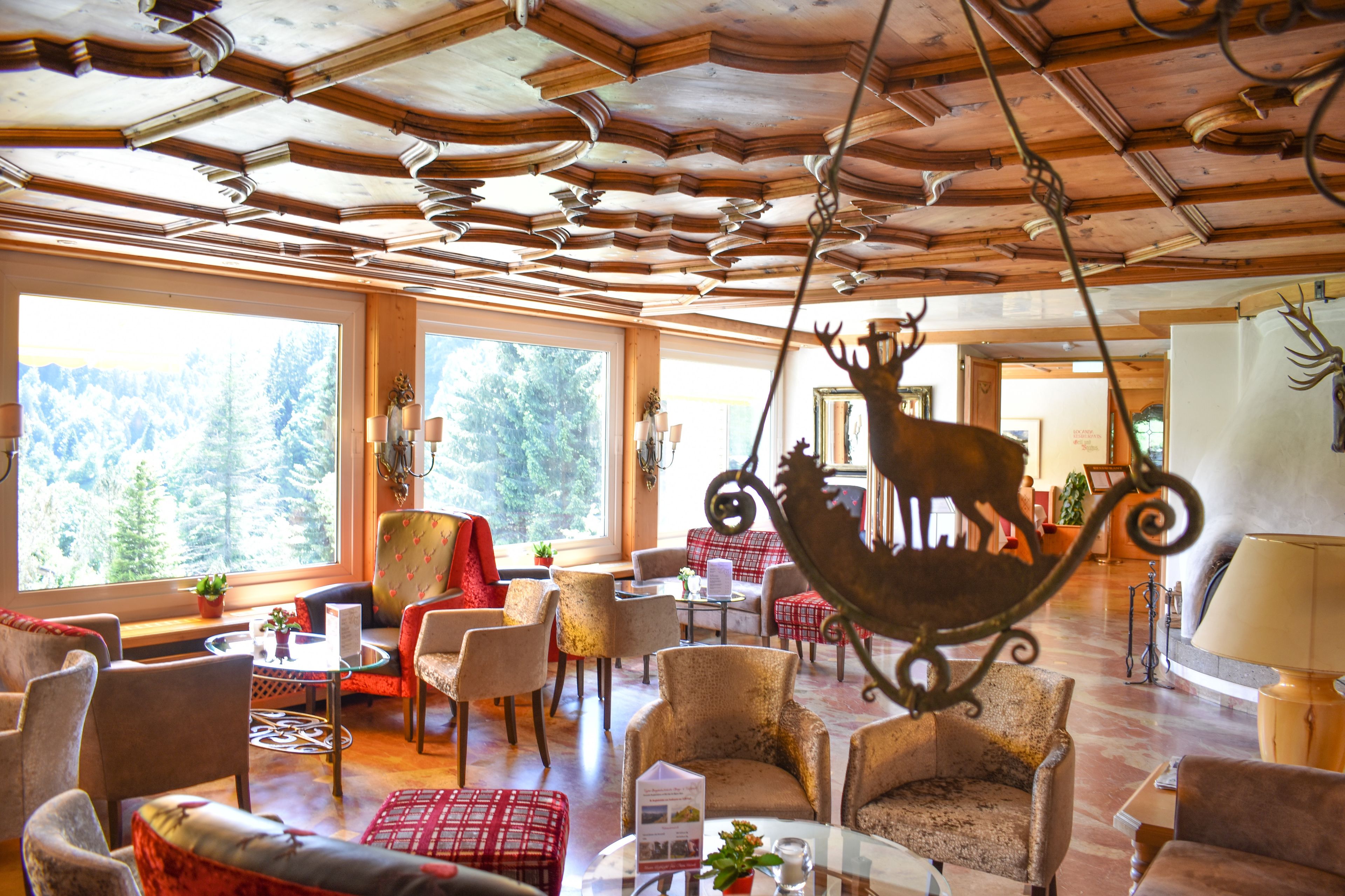A spacious lobby with wooden ceiling beams, comfortable seating, and large windows offering a view of the forest.