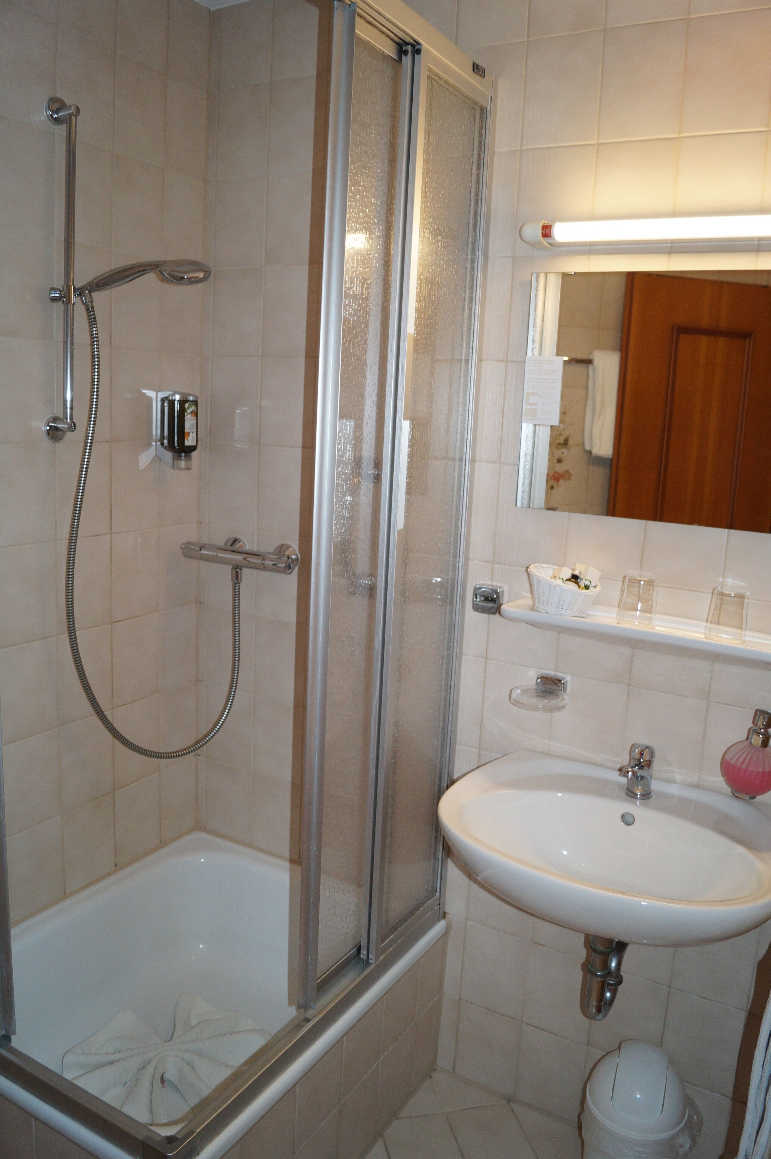 Un baño con cabina de ducha de vidrio, un lavabo blanco y un espejo sobre él.