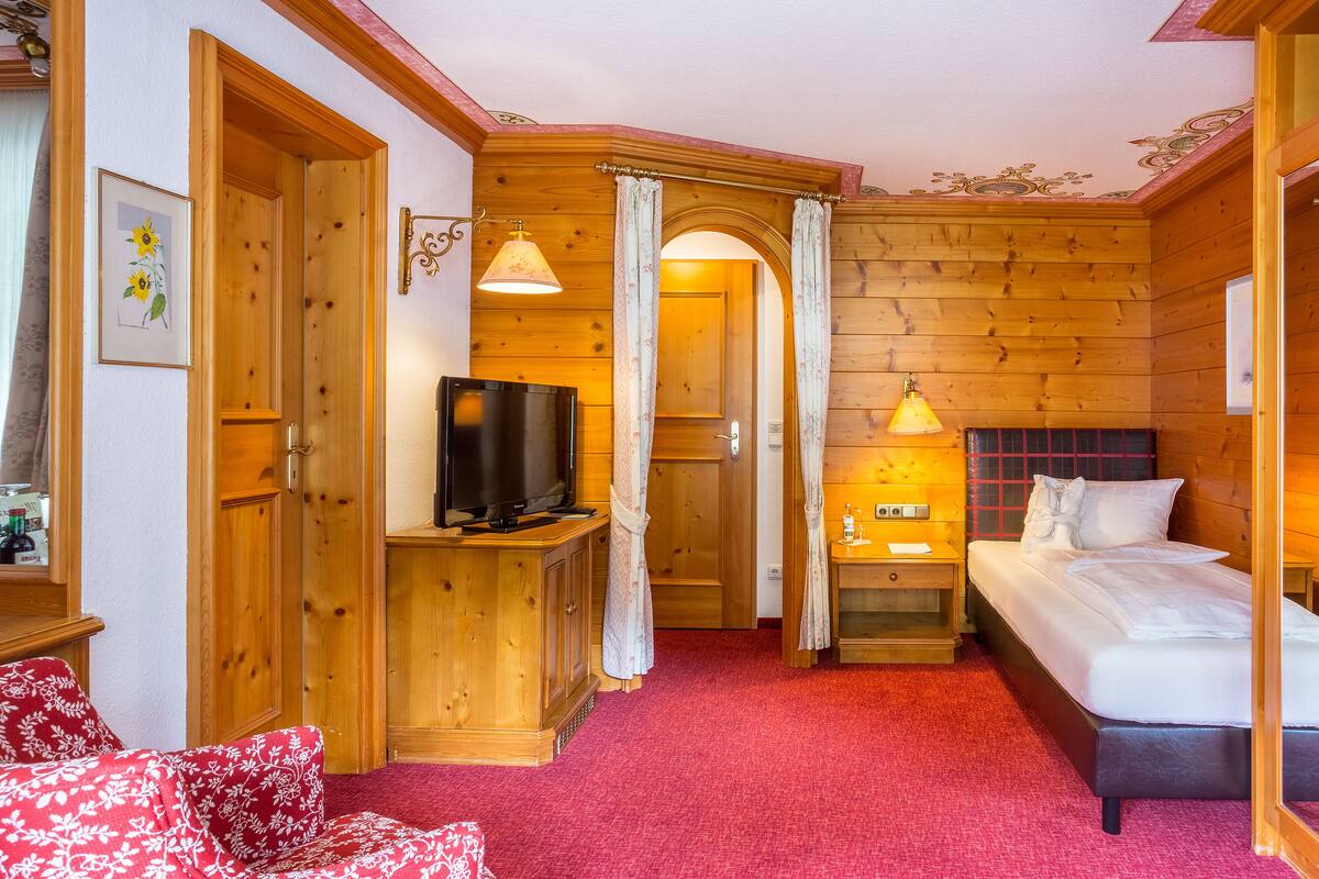 A cozy wooden room with a bed, a TV, and a red carpet.