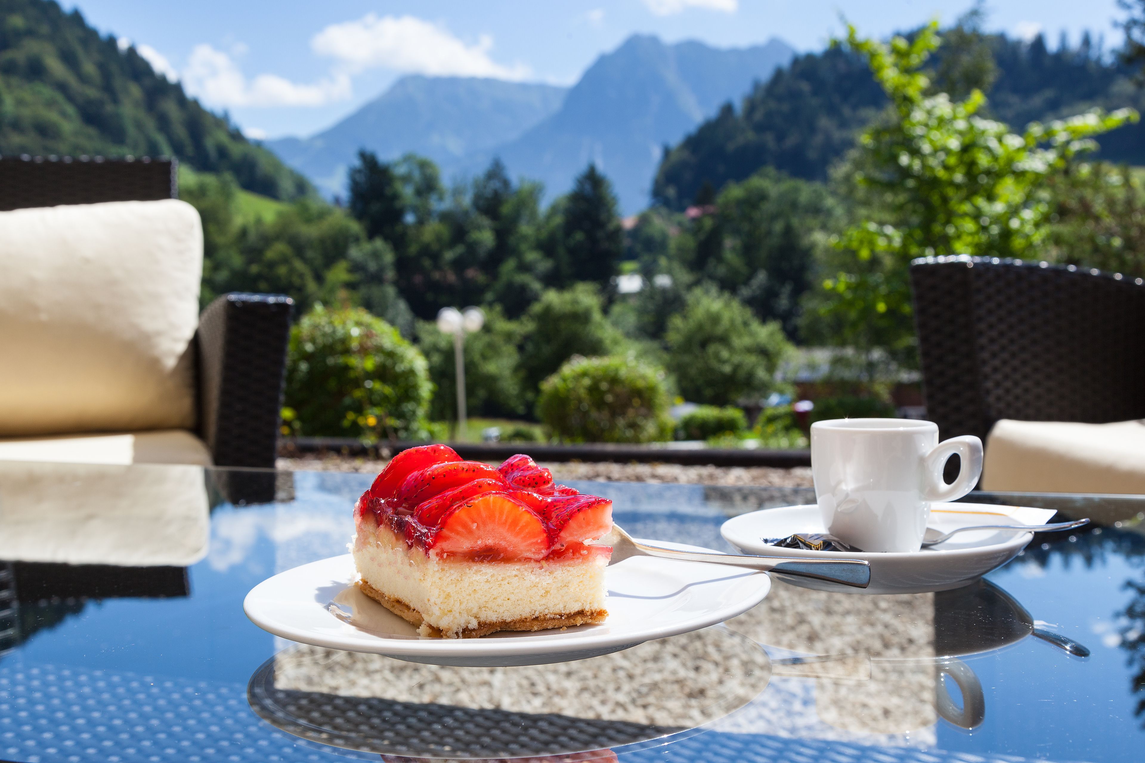 A dessert on a glass table with a cup and saucer beside it, set against a scenic mountain backdrop.
