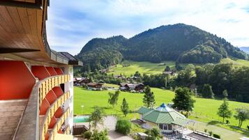 A hotel with a curved roof, a swimming pool, and a view of a green valley with houses and trees.