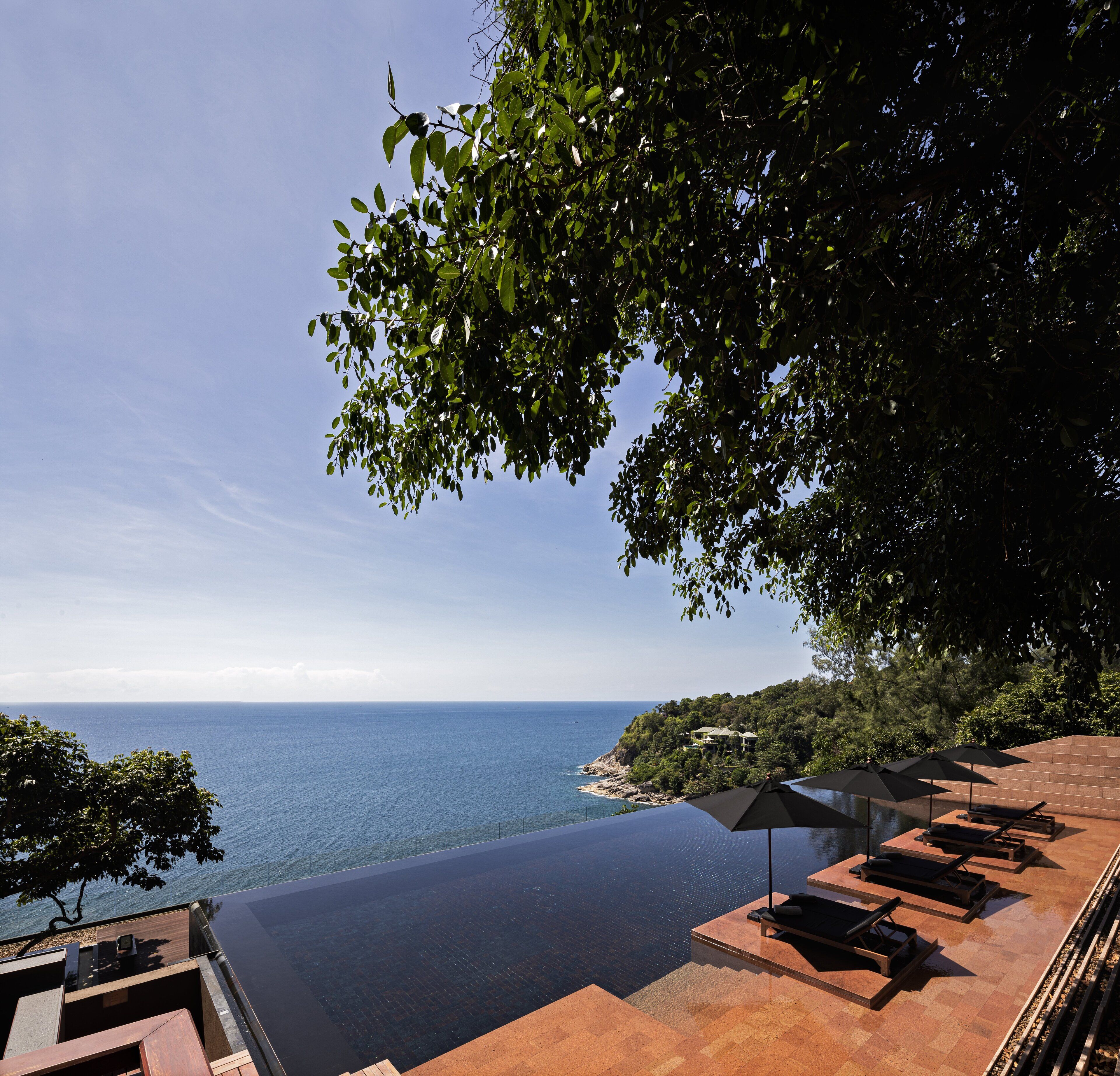 Une piscine à débordement luxueuse, offrant une vue imprenable sur la mer, avec des chaises longues et des parasols, et donnant sur une propriété située en bord de mer.
