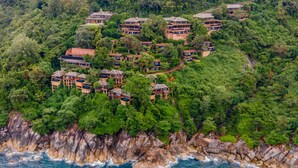 A coastal resort with multiple bungalow-style buildings nestled among dense greenery, overlooking the ocean.
