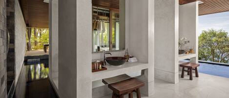 A modern bathroom with a large sink, wooden stools, and a view of a swimming pool.
