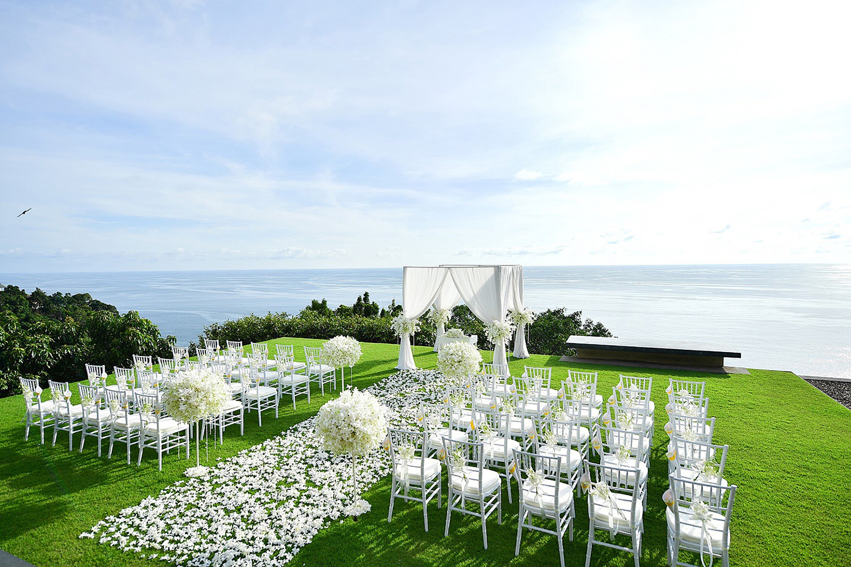 An outdoor wedding setup with white chairs and a white canopy, overlooking a body of water.