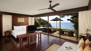 A bedroom with a large bed, a TV, a wooden desk, and a view of the ocean through large glass doors. - Paresa Resort Phuket (Kamala)